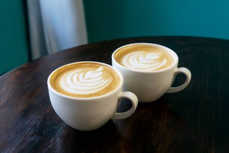 Two cups of cappuccino with latte art on brown wooden background. Perfect foam, place for text.の写真素材