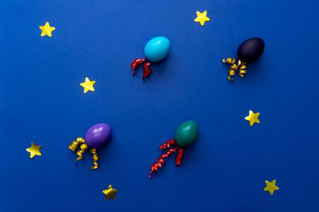Color easter eggs as rockets over blue background. Easter festive cosmic concept. Flat lay.の写真素材