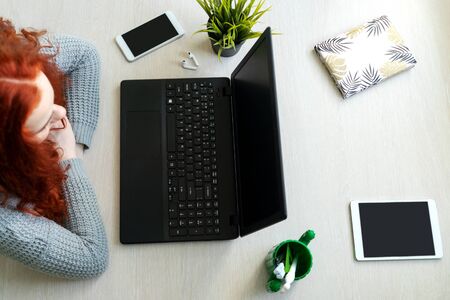 Office life. Young red-haired woman and workplace. Flat lay. Note pad, laptop, phone and tablet around girl. Top view.の写真素材