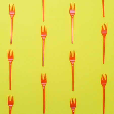 Plastic red forks on yellow background.