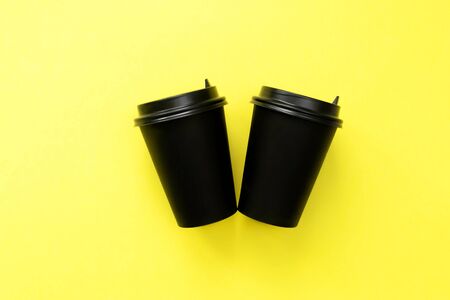 Two disposable coffee cup on yellow background. Black craft glass for coffee or tea.の写真素材