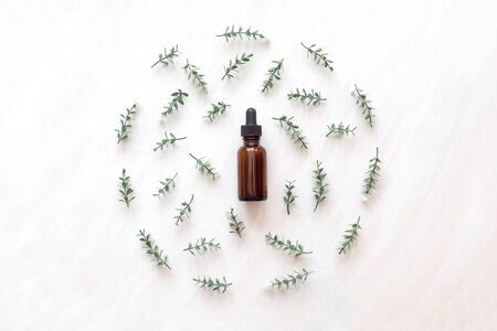 top view of bottle with natural oil in frame of branches with little flowers on white wooden background.の写真素材