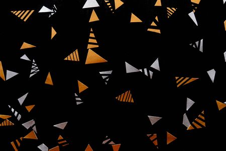 Golden and silver triangle confetti isolated on black background.