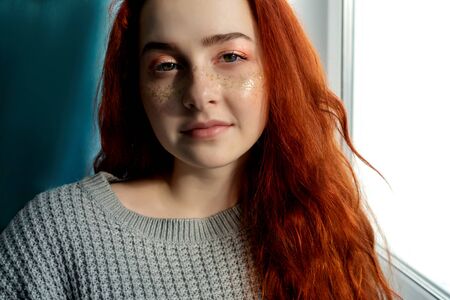 Pretty red- haired woman near window. Perfect make up with sparkles.の写真素材