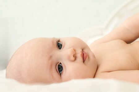 Naked cute baby girl lie on a light background in bed. At home.