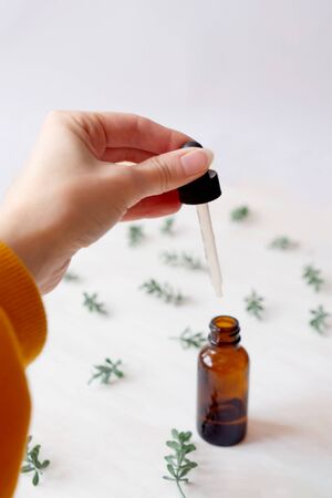 Front view of hand with pipette and bottle with natural oil on white wooden background. Green plants.の写真素材