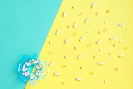 Days of the week pill box on yellow and turquoise. Flat lay, copy space.の写真素材