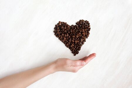 heart of cofee grains from the hand on white wooden backgroundの写真素材