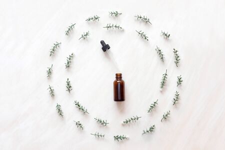 top view of bottle with natural oil in frame of branches with little flowers on white wooden background.の写真素材
