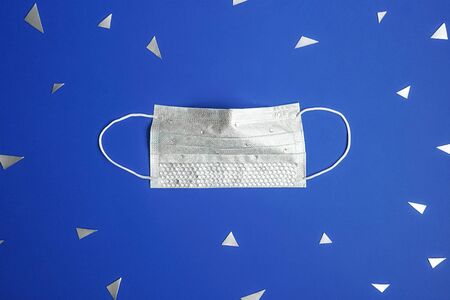 Medical mask over hand with rhinestones on blue background. Epidemic concept, flat lay. Triangular confetti around.の写真素材