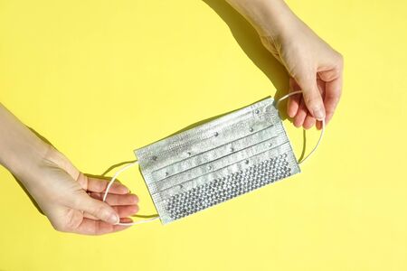 Medical mask with rhinestones in hands on yellow background. Epidemic concept, flat lay.の写真素材