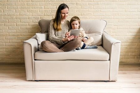 Mother and son in casual clothes on sofa use laptop. Lockdown concept, technology.の写真素材