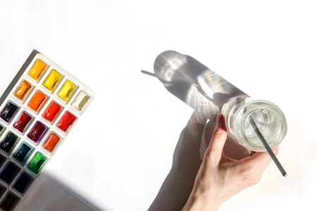 Hand with glass jar and brush, watercolor paints on white. Art concept, copy space.の写真素材