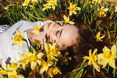 Portrait of young red-haired beautiful girl lying on narcissus. Front view. Concept of spring and summer youth happiness.の写真素材