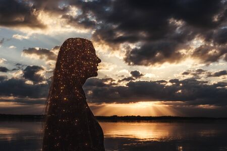 Silhouette of woman. Sun rays from clouds. Sunset on river.