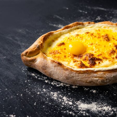 Part of Khachapuri adjara traditional Georgian cuisine meal. Baked bread as boat with cheese and egg filling on black background, decorated with flour. National pastry snack.の写真素材