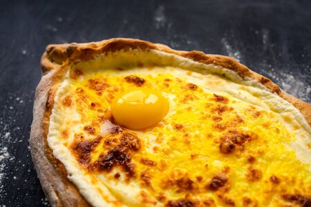 Khachapuri adjara traditional Georgian cuisine meal. Baked bread as boat with cheese and egg filling on black background. Part of khachapuri, close up.の写真素材