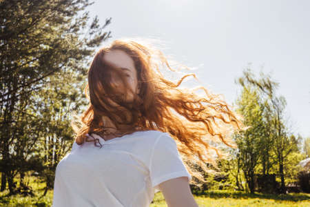 Young happy ginger girl with long curly hair in sunshine. Country life. Hair over face.