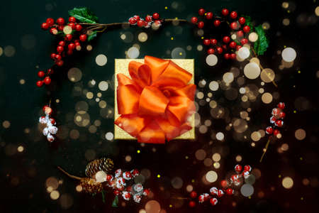 Gift box with red bow and berries branches. Black background decorated with stars confetti and...