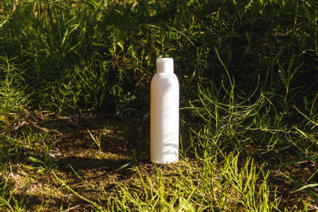 White bottle on green natural background. Cosmetic or bottle of water, ecological concept. Grass,...