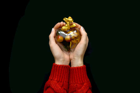 Transparent heart with Christmas composition inside in hands on black background. Top view.の写真素材
