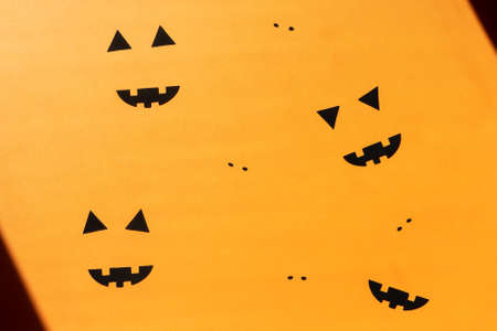 Flat lay Halloween background with decorative pumpkin and ghost faces on orange backdrop. Festive...