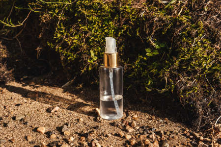 Glass cosmetic bottle with oil stand in the brown sand with moss background, sunlight. The concept of natural cosmetics, natural essential oil.の写真素材