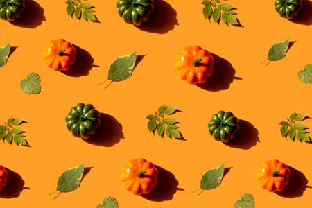 Autumn pattern with various pumpkins and dried leaves on orange background, top view. Halloween and autumn concept, greeting card.の写真素材