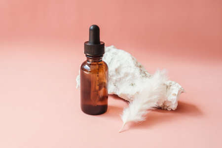 Blank amber glass essential oil bottle on beige background. Natural organic cosmetics, alternative medicine, sustainable lifestyle concept. Front view, copy space. Decor with stones, aer. Minimalism.の写真素材