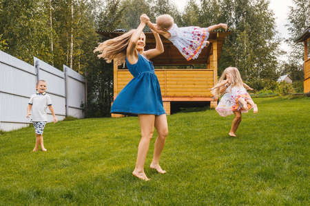 Happy kids and mother playing in garden on grass. Summer time.