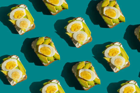Healthy lunch snack. Bright pattern from delicious avocado sandwiches made with fresh sliced avocados on turquoise background, top view, flat lay.の写真素材