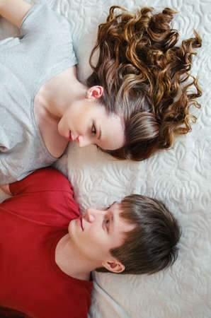 Young attractive couple wake up in bed and look each other. Top view.