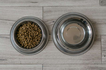 Bowl with dry food and water for pet, dogs or cats on gray floor background. Top view.