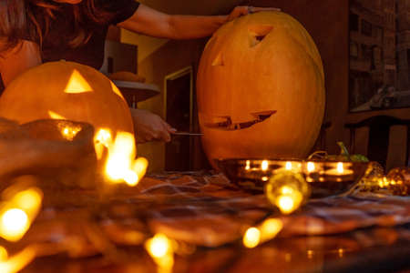 Halloween pumpkins and big spider with electric illumination on table. Womans hands carving pumpkin.の写真素材