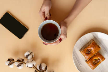 Perfect breakfast: baklava on marble plate and cup of black coffee. Flat lay with cotton plant, phone and hands.の写真素材
