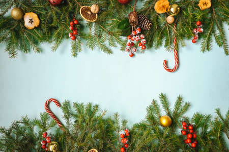 Christmas frame with fir and christmas baubles, red berry on blue background. Copy space.