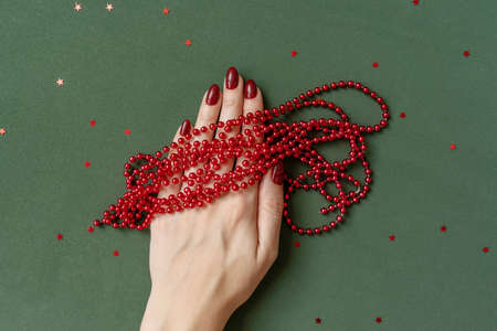 Christmas manicure. Red nails, hand with red beads on green background with red stars.の写真素材
