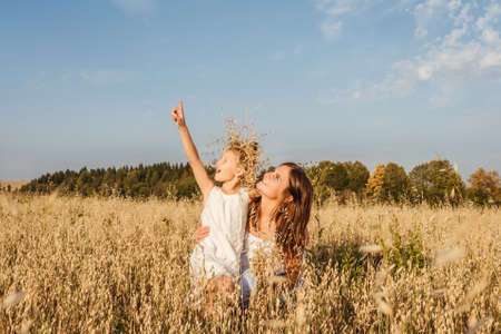 Beautiful young mother and her daughter look up and show with finger to sky. White clothes, freedom concept. Copy space, fromt view.の写真素材