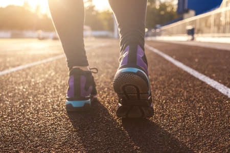 Runner feet running on stadium tracks closeup on shoe. Woman fitness sunset jog workout welness...