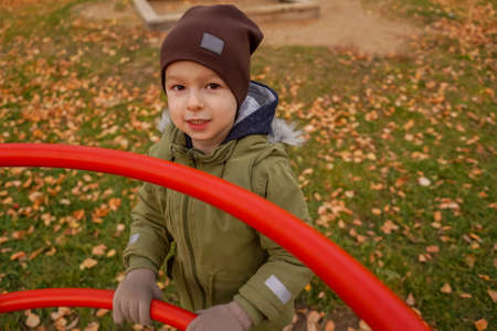 Young happy toddler boy stand on walk, autumn. Top view, shot through the red playground.
