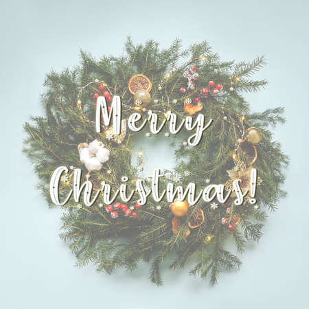 Christmas composition. Handmade christmas wreath from fir branches. Top view, flat lay. Blue background, berries, orange and apple slices as decoration. Merry christmas lettering.の写真素材