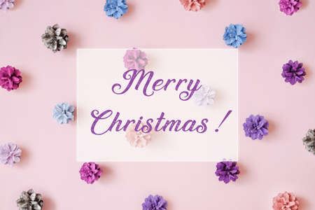Multi-colored Christmas tree cones pattern on pink background. Merry Christmas lettering. Flat lay style.の写真素材