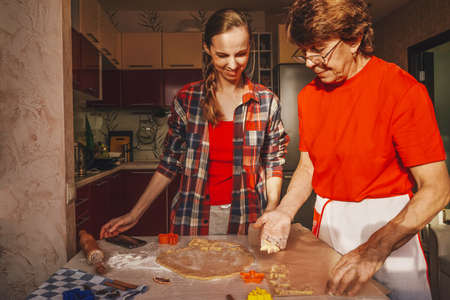 Young woman and senior mother cooking cookies in red clothes.の写真素材