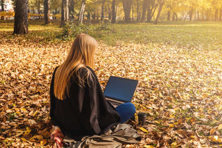 Young businesswoman working on nature with coffee. Autumn park, sunny day. Top view.の写真素材