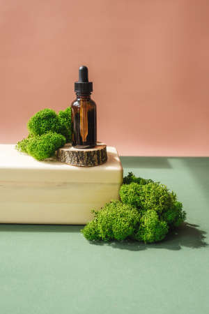 Blank amber glass essential oil bottle on wooden brick. Natural organic cosmetics, herbal essence, sustainable lifestyle concept. Front view, copy space. Decor with moss, saw cut.の写真素材