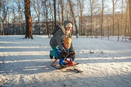 In winter, happy mom and son ride a snow scooter from the mountain in white snow.の写真素材