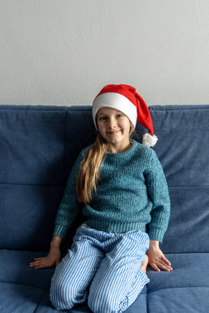 Little girl in santa hat on the blue sofa at home.の写真素材