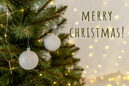 Part of Christmas tree with white balls, Christmas lights garlands on white brick wall on background. Merry christmas lettering.の写真素材