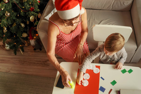 A Little boy with grandmother make Christmas craft, greeting card. Christmas tree and decoration on background. Top view.の写真素材