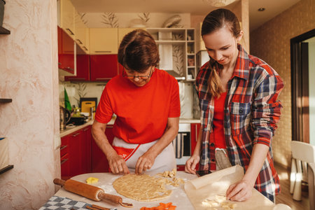 Young woman and senior mother cooking cookies in red clothes.の写真素材